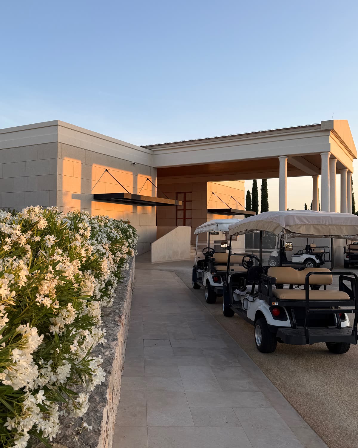 The entrance of Amanzoe at dusk, white oleanders along the path and golf carts waiting under the portico