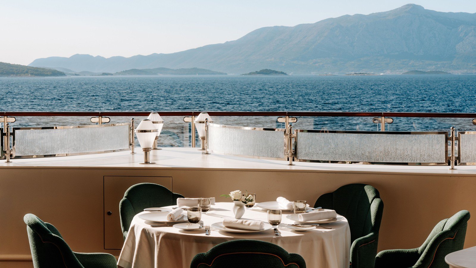 A table set for lunch on the open deck of a Four Seasons yacht, looking out over the sea to the mountains